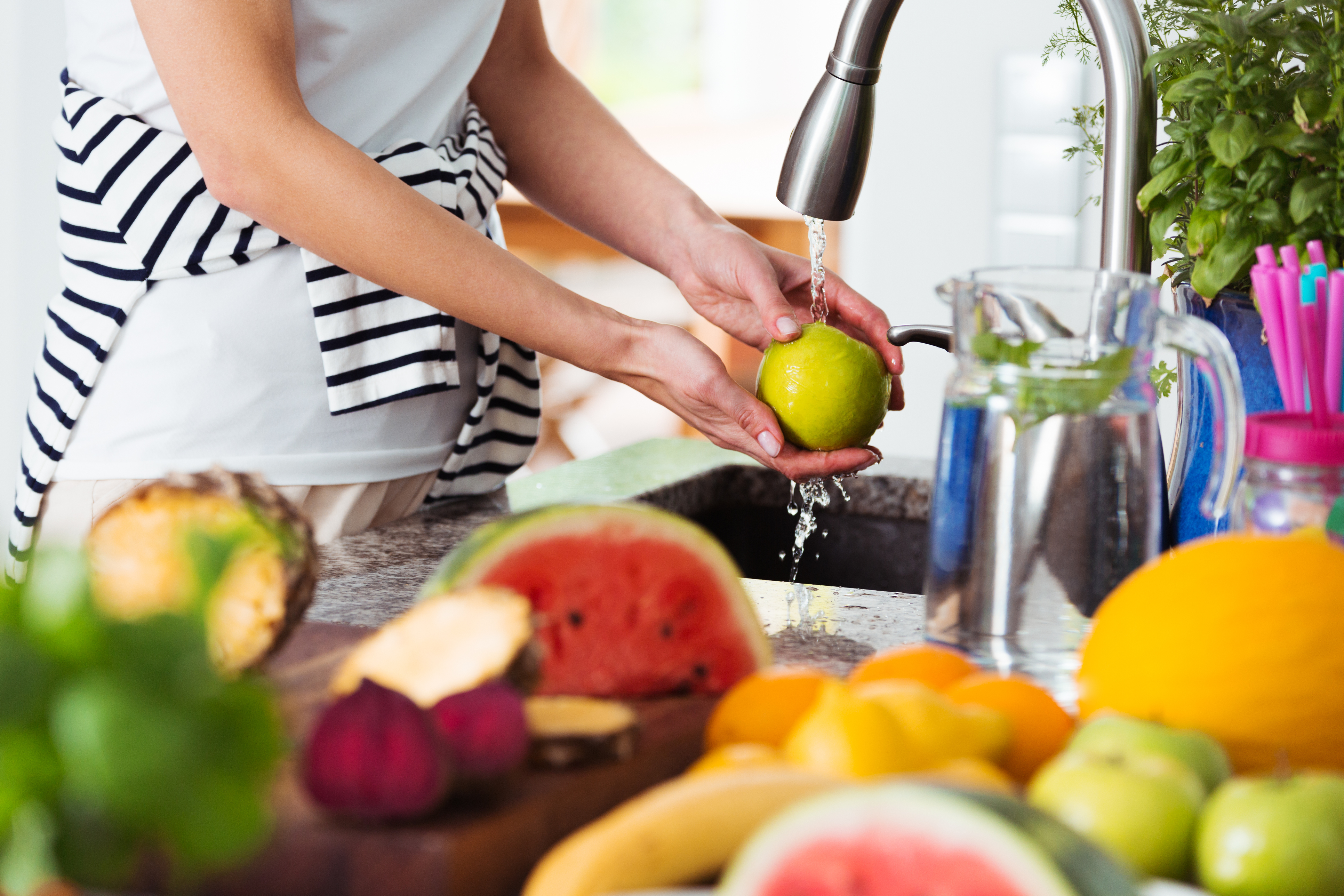 Healthy woman washing apple above kitchen sink while preparing fresh breakfast with fruits